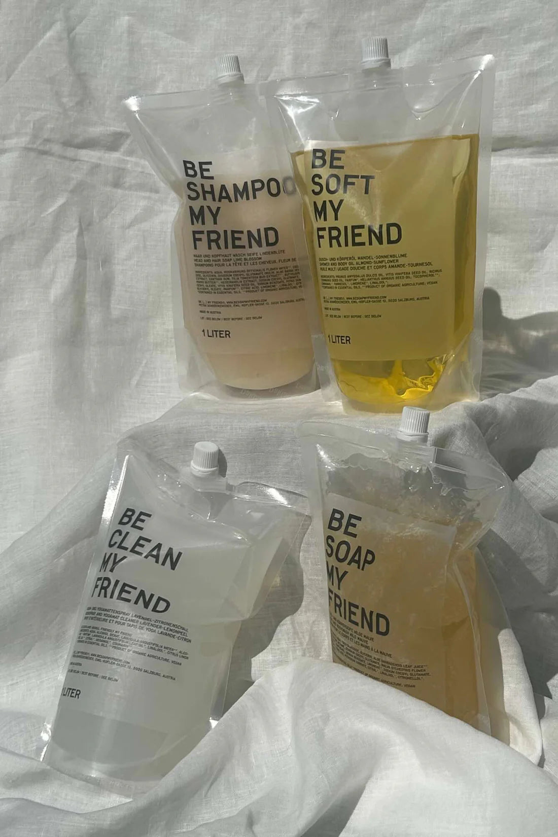 Four transparent refill pouches with beige and yellow hair care liquids labeled "Be Shampoo My Friend," "Be Soft My Friend," .