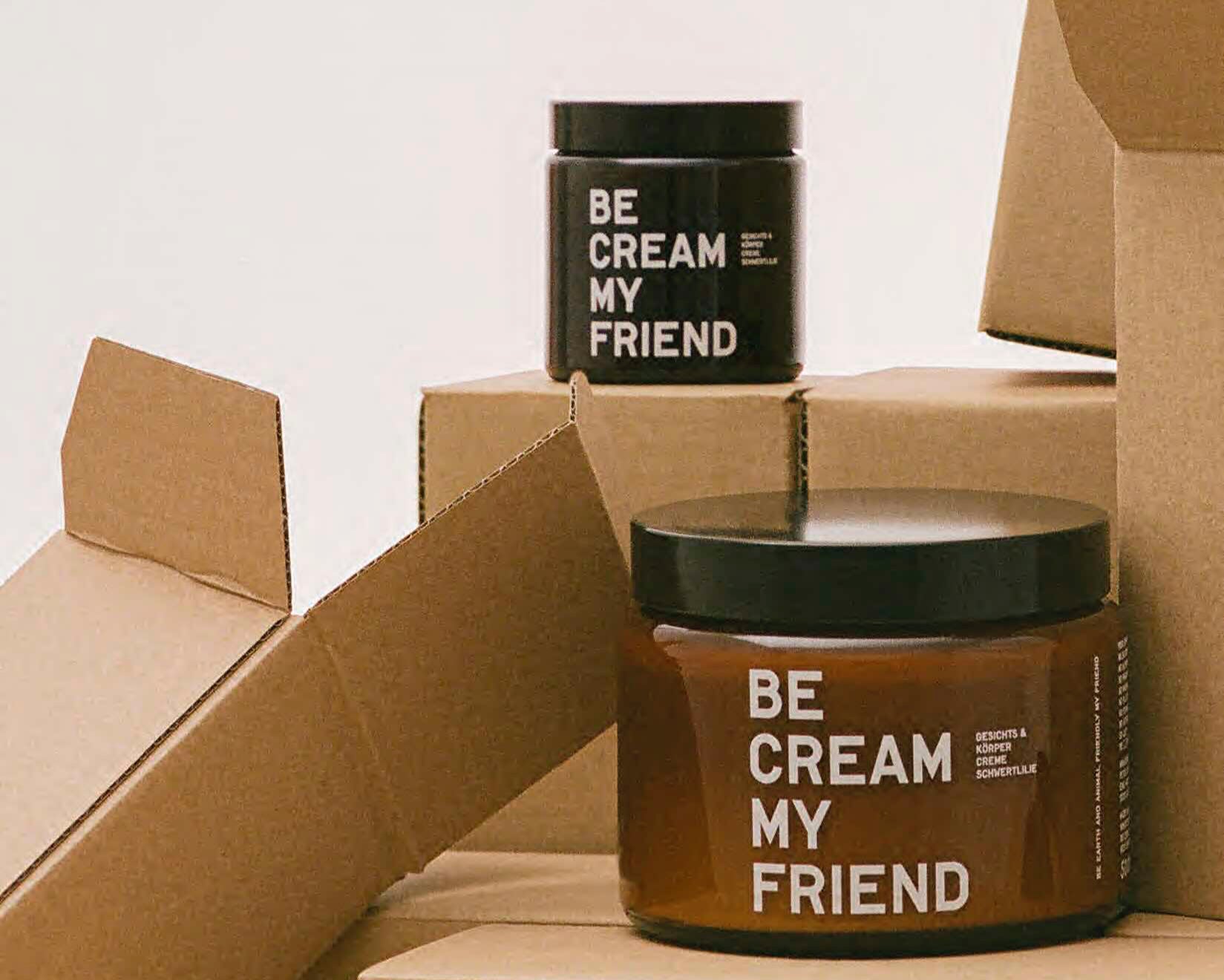 Brown glass jar and black plastic refill container labeled "Be Cream My Friend" inside partially opened cardboard boxes.