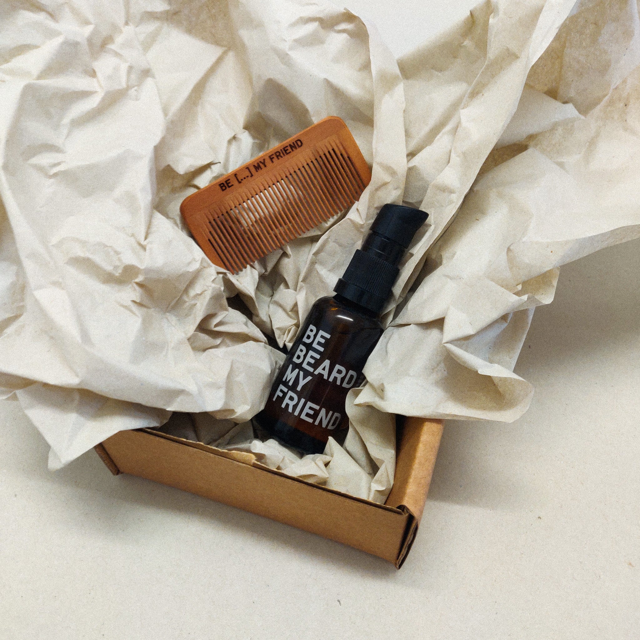 Wooden beard comb and black spray bottle with "Beard My Friend" text in cardboard gift box with crumpled paper filler.