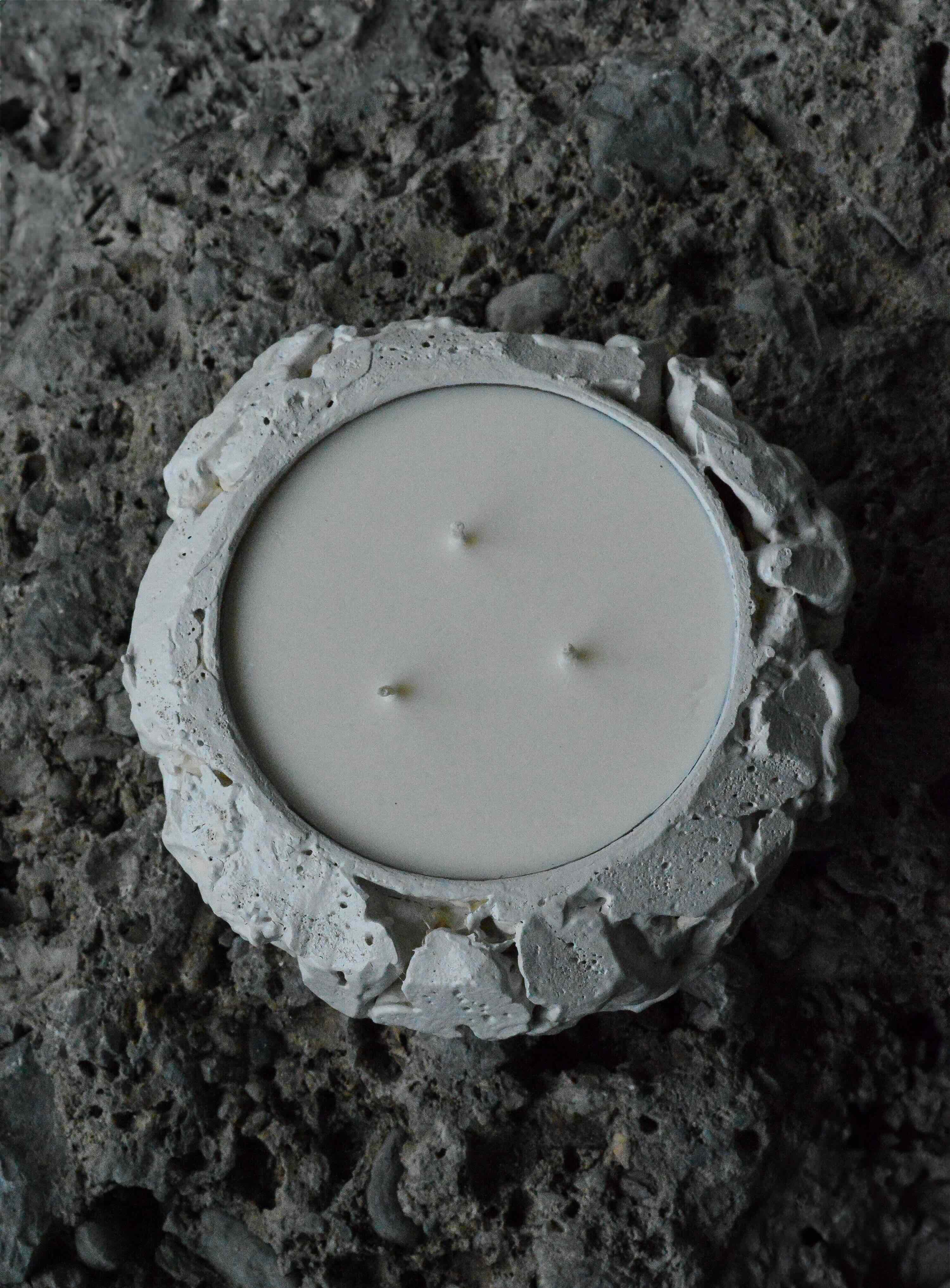 White three-wick candle in textured, rough-edged stone holder on dark stone surface.