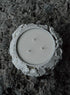 White three-wick candle in textured, rough-edged stone holder on dark stone surface.