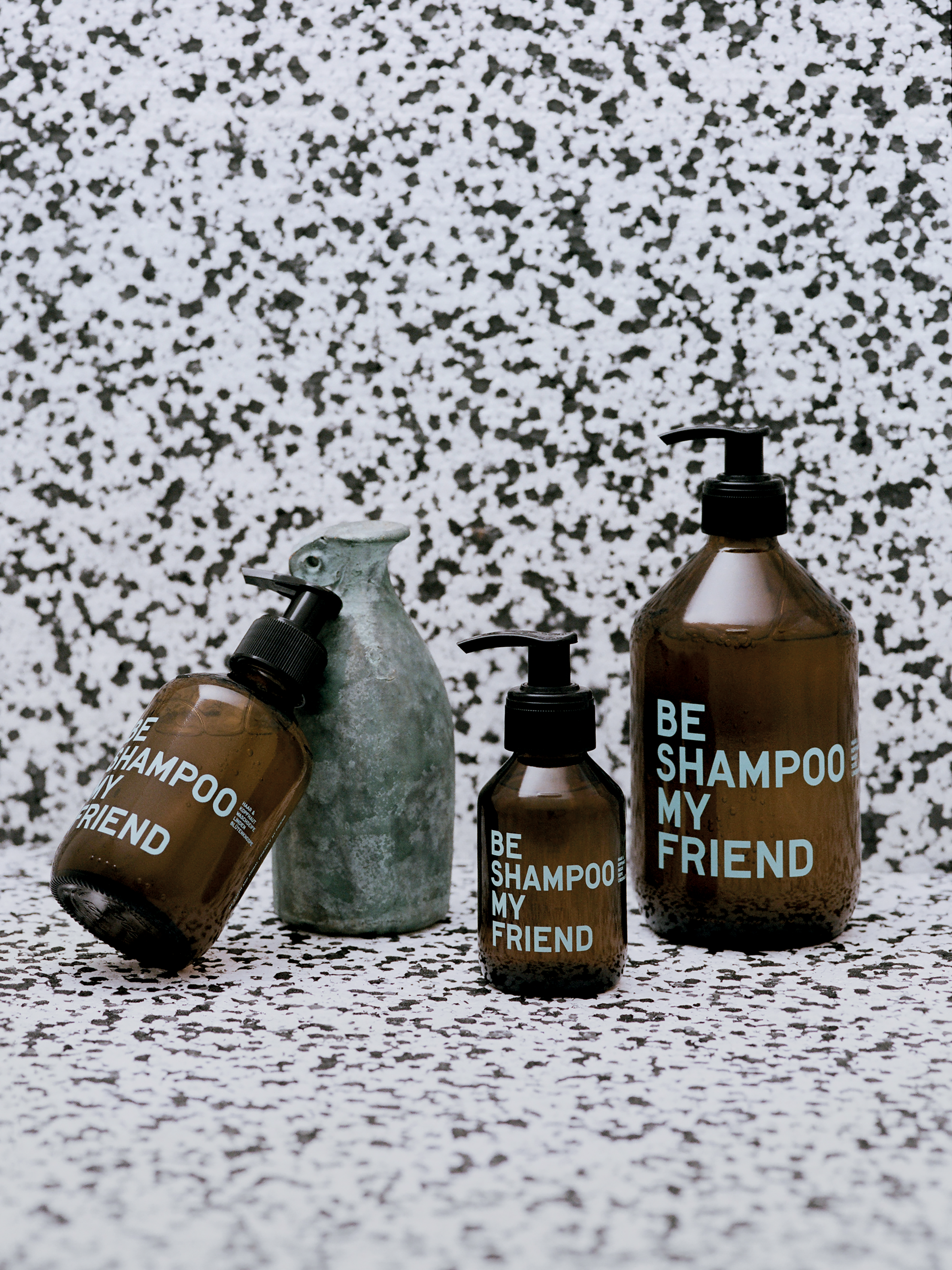 Brown bottles with black pump dispensers labeled "BE SHAMPOO MY FRIEND" and "SHAMPOO FRIEND" against a speckled white and.