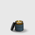 Amber glass candle jar with burning wick and dark blue label reading Botanical Blend, black lid beside jar.