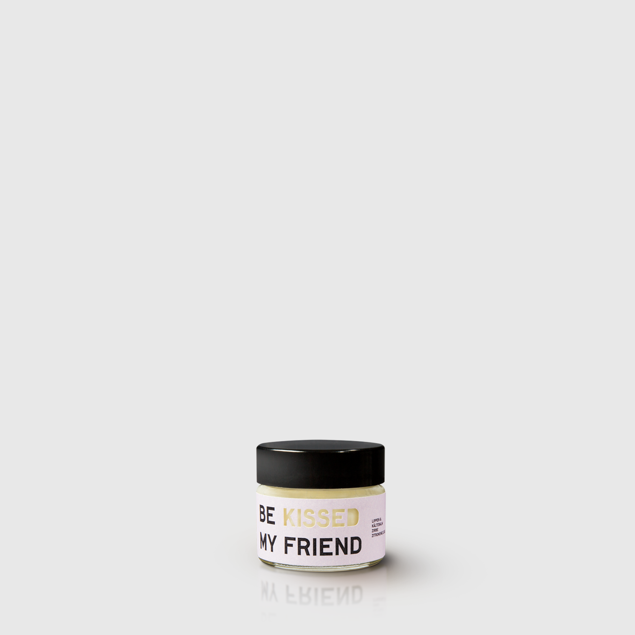 Small round white candle jar with black lid and gold text "BE KISSED MY FRIEND" on the label.
