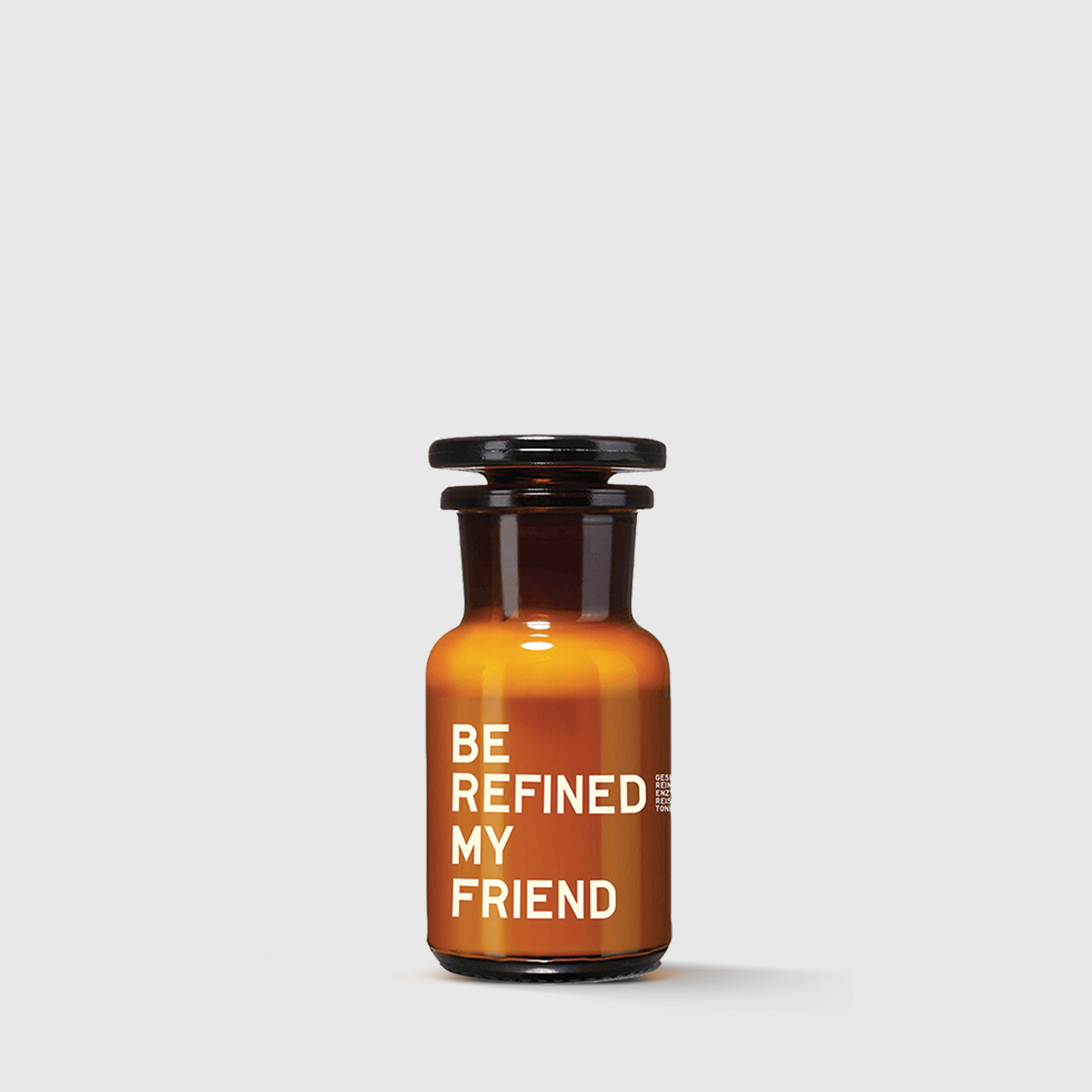 Amber glass jar with black stopper labeled "Be refined my friend" against white background.