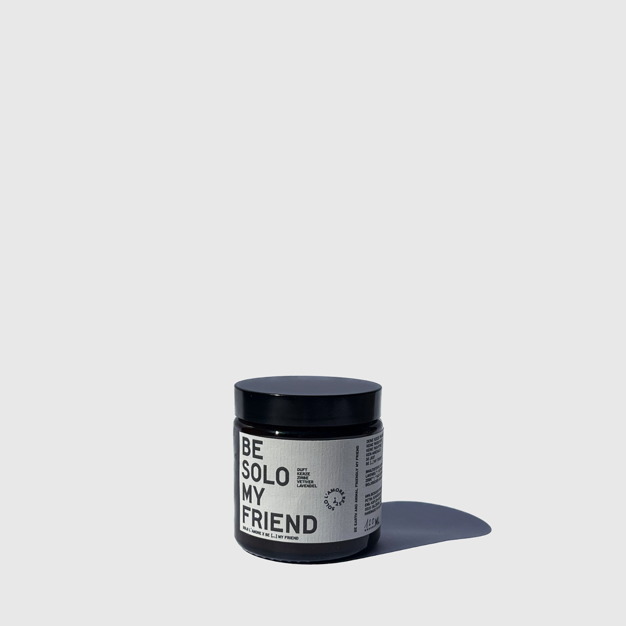 Small dark glass candle jar with black lid and minimalist white label reading "Be Solo My Friend".