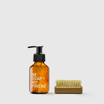 Amber glass soap dispenser with black pump and natural bristle hand brush on wooden base.